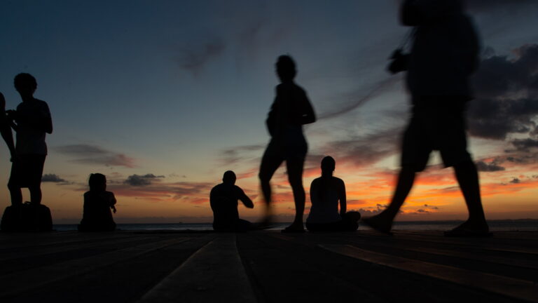 People in silhouette enjoy the dramatic sunset at the pier of Po
